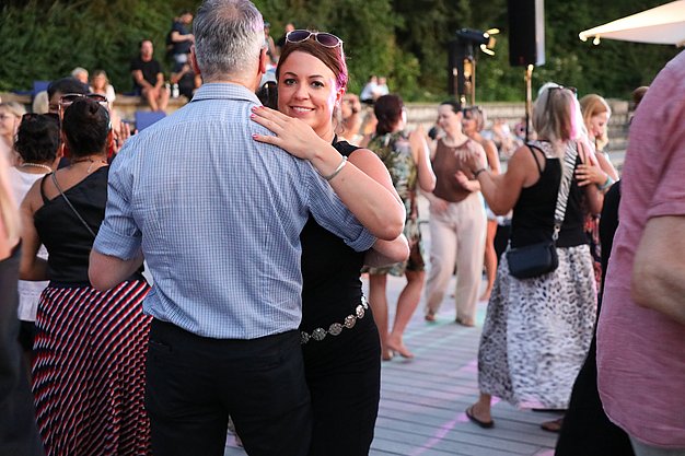 Die Diashow zeigt Eindrücke vom Salsa-Abend am Eckert Beach. Zu sehen sind tanzende Paare, Besucherinnen und Besucher im Publikum sowie die stimmungsvolle Atmosphäre der Veranstaltung am Abend.