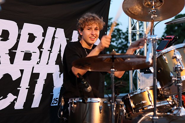 Die Bilder zeigen Eindrücke der Rock-Nacht am Eckert Beach. Zu sehen sind die Live-Auftritte der Bands Rusty Road Runners und ACBarbingCity´25, zahlreiche Besucherinnen und Besucher vor der Bühne sowie die sommerliche Atmosphäre am Strand. In beiden Bands stehen auch Dozenten der Eckert Schulen auf der Bühne. Die Aufnahmen zeigen Musiker, Publikum und die stimmungsvolle Beleuchtung während des Open-Air-Konzerts.