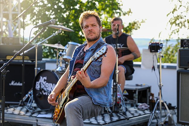 Die Bilder zeigen Eindrücke der Rock-Nacht am Eckert Beach. Zu sehen sind die Live-Auftritte der Bands Rusty Road Runners und ACBarbingCity´25, zahlreiche Besucherinnen und Besucher vor der Bühne sowie die sommerliche Atmosphäre am Strand. In beiden Bands stehen auch Dozenten der Eckert Schulen auf der Bühne. Die Aufnahmen zeigen Musiker, Publikum und die stimmungsvolle Beleuchtung während des Open-Air-Konzerts.