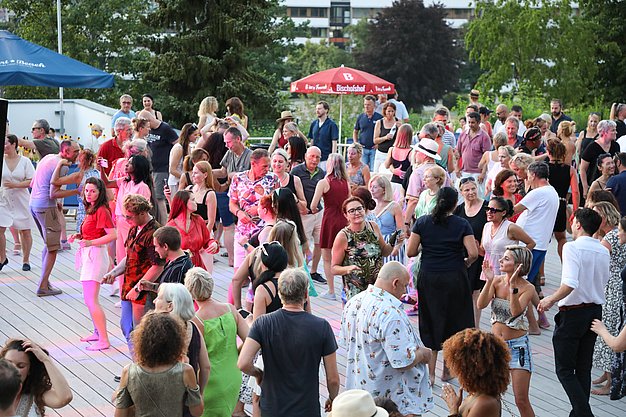 Die Diashow zeigt Eindrücke vom Salsa-Abend am Eckert Beach. Zu sehen sind tanzende Paare, Besucherinnen und Besucher im Publikum sowie die stimmungsvolle Atmosphäre der Veranstaltung am Abend.