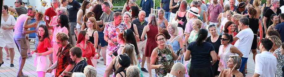 Die Diashow zeigt Eindrücke vom Salsa-Abend am Eckert Beach. Zu sehen sind tanzende Paare, Besucherinnen und Besucher im Publikum sowie die stimmungsvolle Atmosphäre der Veranstaltung am Abend.