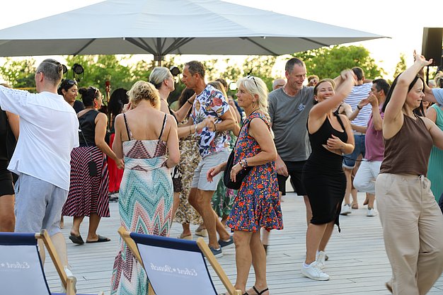 Die Diashow zeigt Eindrücke vom Salsa-Abend am Eckert Beach. Zu sehen sind tanzende Paare, Besucherinnen und Besucher im Publikum sowie die stimmungsvolle Atmosphäre der Veranstaltung am Abend.