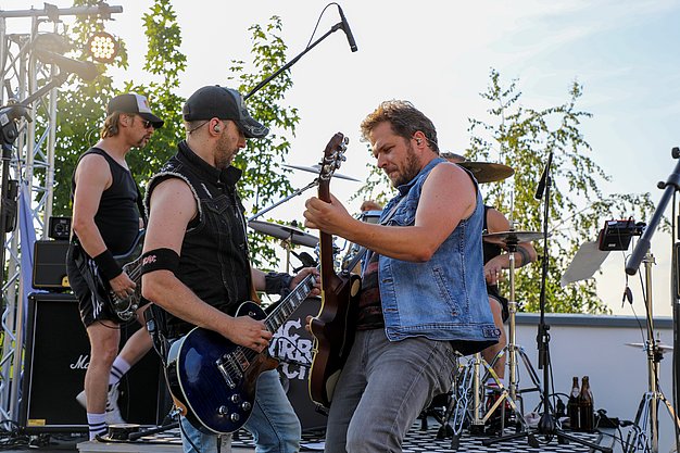 Die Bilder zeigen Eindrücke der Rock-Nacht am Eckert Beach. Zu sehen sind die Live-Auftritte der Bands Rusty Road Runners und ACBarbingCity´25, zahlreiche Besucherinnen und Besucher vor der Bühne sowie die sommerliche Atmosphäre am Strand. In beiden Bands stehen auch Dozenten der Eckert Schulen auf der Bühne. Die Aufnahmen zeigen Musiker, Publikum und die stimmungsvolle Beleuchtung während des Open-Air-Konzerts.