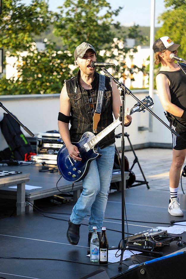Die Bilder zeigen Eindrücke der Rock-Nacht am Eckert Beach. Zu sehen sind die Live-Auftritte der Bands Rusty Road Runners und ACBarbingCity´25, zahlreiche Besucherinnen und Besucher vor der Bühne sowie die sommerliche Atmosphäre am Strand. In beiden Bands stehen auch Dozenten der Eckert Schulen auf der Bühne. Die Aufnahmen zeigen Musiker, Publikum und die stimmungsvolle Beleuchtung während des Open-Air-Konzerts.