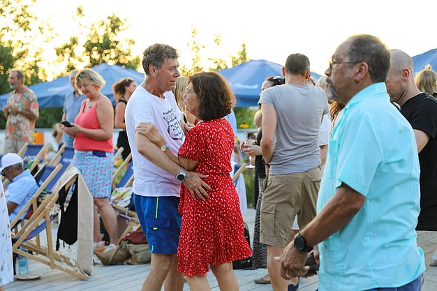 Die Diashow zeigt Eindrücke vom Salsa-Abend am Eckert Beach. Zu sehen sind tanzende Paare, Besucherinnen und Besucher im Publikum sowie die stimmungsvolle Atmosphäre der Veranstaltung am Abend.