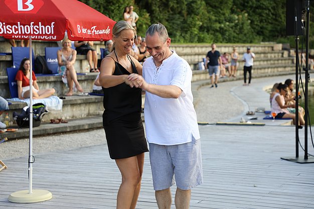 Die Diashow zeigt Eindrücke vom Salsa-Abend am Eckert Beach. Zu sehen sind tanzende Paare, Besucherinnen und Besucher im Publikum sowie die stimmungsvolle Atmosphäre der Veranstaltung am Abend.