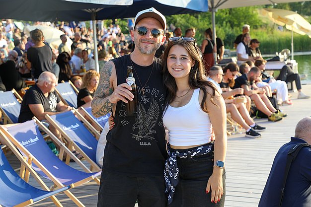 Die Bilder zeigen Eindrücke der Rock-Nacht am Eckert Beach. Zu sehen sind die Live-Auftritte der Bands Rusty Road Runners und ACBarbingCity´25, zahlreiche Besucherinnen und Besucher vor der Bühne sowie die sommerliche Atmosphäre am Strand. In beiden Bands stehen auch Dozenten der Eckert Schulen auf der Bühne. Die Aufnahmen zeigen Musiker, Publikum und die stimmungsvolle Beleuchtung während des Open-Air-Konzerts.