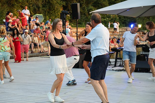 Die Diashow zeigt Eindrücke vom Salsa-Abend am Eckert Beach. Zu sehen sind tanzende Paare, Besucherinnen und Besucher im Publikum sowie die stimmungsvolle Atmosphäre der Veranstaltung am Abend.