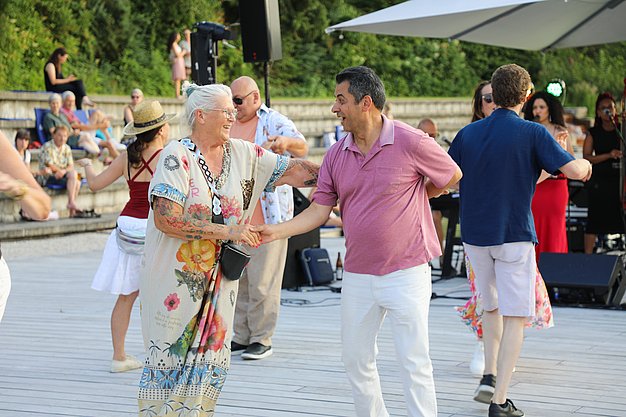 Die Diashow zeigt Eindrücke vom Salsa-Abend am Eckert Beach. Zu sehen sind tanzende Paare, Besucherinnen und Besucher im Publikum sowie die stimmungsvolle Atmosphäre der Veranstaltung am Abend.