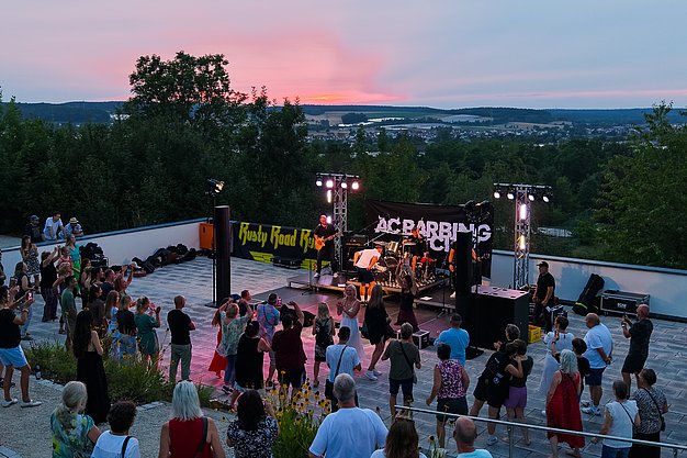 Die Bilder zeigen Eindrücke der Rock-Nacht am Eckert Beach. Zu sehen sind die Live-Auftritte der Bands Rusty Road Runners und ACBarbingCity´25, zahlreiche Besucherinnen und Besucher vor der Bühne sowie die sommerliche Atmosphäre am Strand. In beiden Bands stehen auch Dozenten der Eckert Schulen auf der Bühne. Die Aufnahmen zeigen Musiker, Publikum und die stimmungsvolle Beleuchtung während des Open-Air-Konzerts.