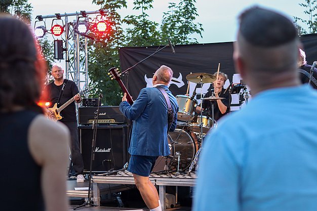 Die Bilder zeigen Eindrücke der Rock-Nacht am Eckert Beach. Zu sehen sind die Live-Auftritte der Bands Rusty Road Runners und ACBarbingCity´25, zahlreiche Besucherinnen und Besucher vor der Bühne sowie die sommerliche Atmosphäre am Strand. In beiden Bands stehen auch Dozenten der Eckert Schulen auf der Bühne. Die Aufnahmen zeigen Musiker, Publikum und die stimmungsvolle Beleuchtung während des Open-Air-Konzerts.