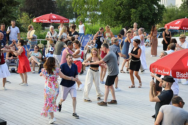 Die Diashow zeigt Eindrücke vom Salsa-Abend am Eckert Beach. Zu sehen sind tanzende Paare, Besucherinnen und Besucher im Publikum sowie die stimmungsvolle Atmosphäre der Veranstaltung am Abend.