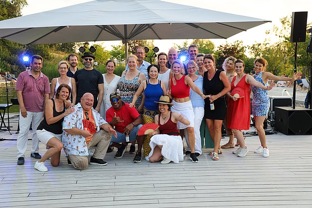 Die Diashow zeigt Eindrücke vom Salsa-Abend am Eckert Beach. Zu sehen sind tanzende Paare, Besucherinnen und Besucher im Publikum sowie die stimmungsvolle Atmosphäre der Veranstaltung am Abend.